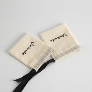 Detail of off-white cotton drawstring jewelry bags with black silk ribbons and logo