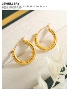 Detailed close-up of 18K gold plated hoop earrings on textured white background