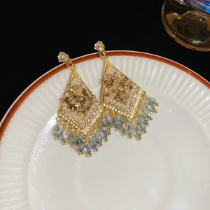 Close-up of diamond-encrusted rhombic tassel earrings on a ceramic dish with blue beads