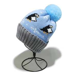 Close-up of winter knit beanie featuring penguin jacquard patterns and a blue faux fur pom