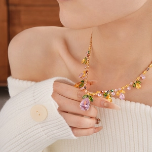 Detail of necklace featuring pink teardrop and green leaf zircons on a gold chain