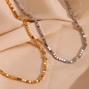 Macro shot of gold and silver cube bead necklaces on elegant champagne silk fabric