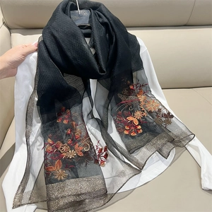 Detailed close-up of a black semi-transparent scarf with floral gold and red embroidery