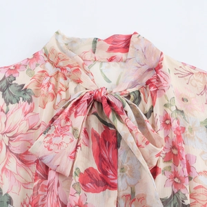 Detailed close-up of chiffon floral dress with elegant bow tie neck and red flower patterns