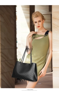 Close-up of black quilted leather tote bag with metallic chain strap worn by a model