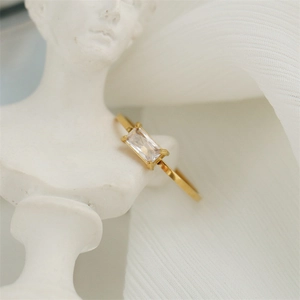 Close-up of an 18K gold plated ring with a rectangular crystal on a white statue