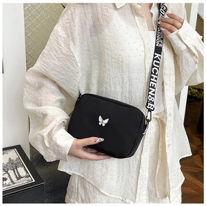 Detail of black nylon crossbody bag with butterfly ornament and lettered wide strap