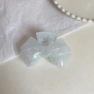 Macro detail of a creamy blue bow hair claw clip made of translucent acrylic on white background