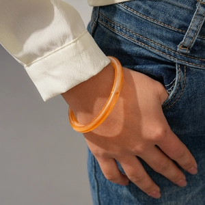 Orange translucent acrylic bangle worn on wrist showing the minimalist round design