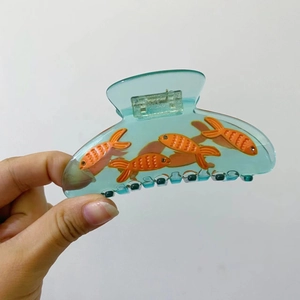 Close-up of translucent blue acetate hair claw clip with orange goldfish patterns