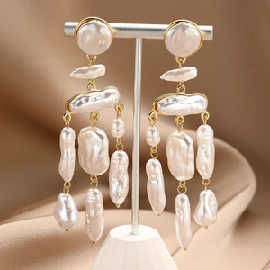Detailed close-up of tiered baroque pearl drop earrings on a golden jewelry stand