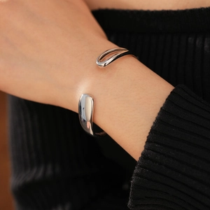 Close-up of polished silver water drop open cuff bracelet worn on wrist with black knit