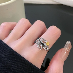 Detail of silver branch ring with NOBLE text and small gold roses on model finger