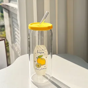 Close-up of glass tumbler with lemon graphics, yellow lid, and glass straw on table