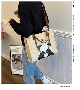 Canvas panda tote bag featuring brown handles and adjustable shoulder strap worn by model