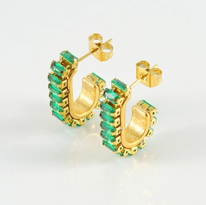 Close-up of golden U-shaped earrings with emerald green zircon stones and reflections