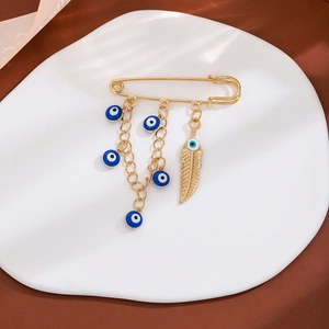Gold evil eye brooch with blue charms and feather tassel on a minimalist display