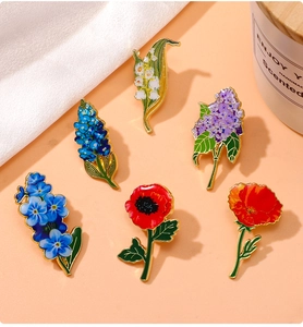 Detail of colorful lily of the valley and lilac flower enamel brooches on peach background