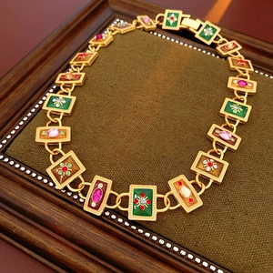 Detail of vintage gold necklace with colorful enamel floral links and gems in wooden frame