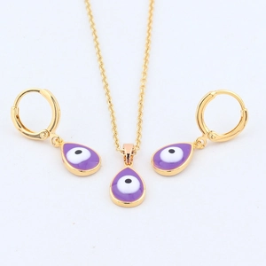 Detailed close-up of golden teardrop necklace and earrings with purple evil eye design