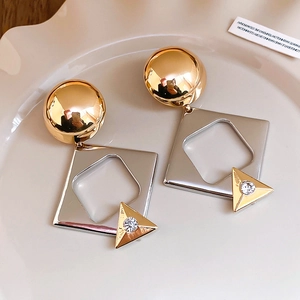 Macro shot of geometric mixed-metal earrings with crystal inlay on a beige plate