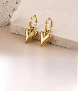 Detail of gold titanium steel hoop earrings with polished heart charms on a stone base
