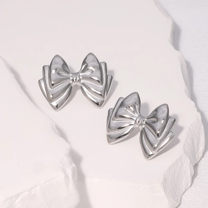 Elegant 3D silver bow earrings in stainless steel on minimalist stone background