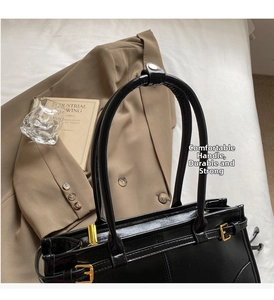 Close-up of black leather tote bag with gold buckle on white soft fabric and beige suit
