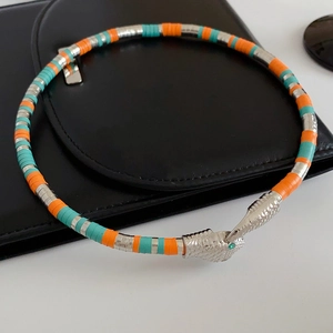 Macro view of silver snake-shaped necklace with turquoise beads and green gemstone eyes