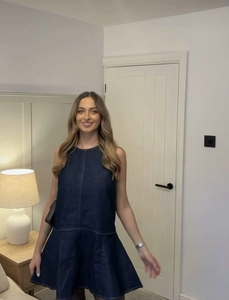 Detailed view of dark blue denim sleeveless dress with round neck and ruffled hemline