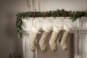 Set of 4 knitted Christmas stockings in oatmeal beige hanging on a white vintage fireplace