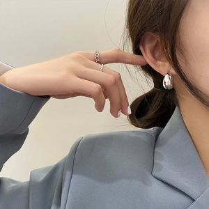 Detail of model wearing silver teardrop earrings and minimalist chain rings with blue blazer