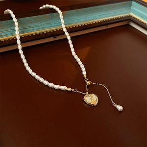 Gros plan du collier de perles avec pendentif cœur doré et perle goutte sur cuir