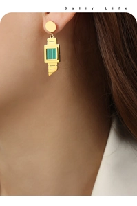 Detail of geometric gold earrings with green textured pendant on a female model