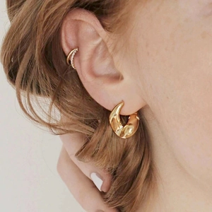 Dettaglio di orecchini a cerchio a C dorati e un ear cuff scintillante su un modello