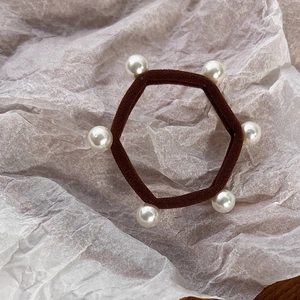 Detail of dark brown elastic hair tie with six white pearls on textured background