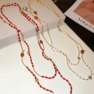 Three long beaded crystal necklaces in red and white with gold accents on a display box