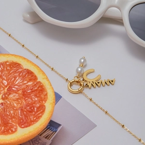 Detailed macro view of a gold MAMA pendant with pearls on a beaded chain necklace