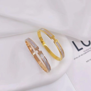 Detailed view of H-letter bangles in gold and rose gold with white shell inlay