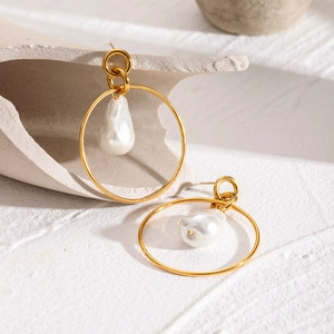 Detail of gold hoop earrings with baroque pearls on a minimalist white textured base