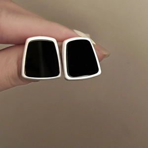 Detail of hand-held geometric black resin earrings with silver metal frame design