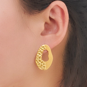 Close-up of golden irregular hollow earrings with hammered texture on female model