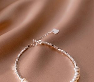 Detailed macro view of S925 sterling silver chain with pearls on champagne silk fabric