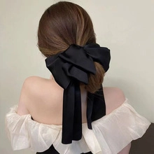 Rear view of a large black silk bow hair clip with long ribbons on a female model