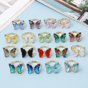 Collection of colorful crystal butterfly rings in gold finish on light blue background