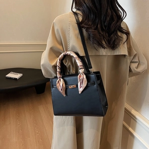 Elegant black leather handbag with a patterned scarf handle shown on a beige trench coat