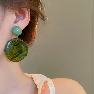 Detail of irregular resin earrings with dark green marble texture worn by a model