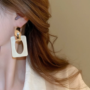 Close-up of geometric resin drop earring with gold metal ring and white hollow pendant