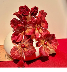 Macro detail of red fabric rose earrings with crystal center on white ceramic