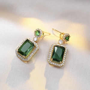 Emerald green rectangle earrings with diamond halo on silk background